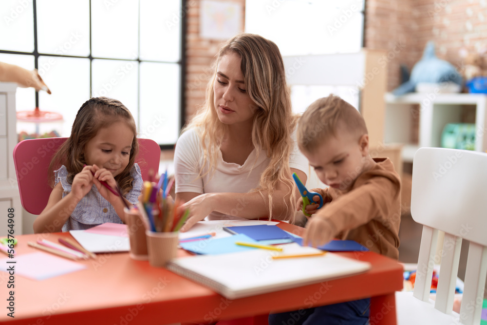 Teacher with boy and girl sitting on table having handcrafts class at kindergarten