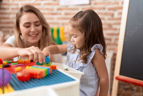 Teacher and toddler playing with construction blocks sitting on table at kindergarten