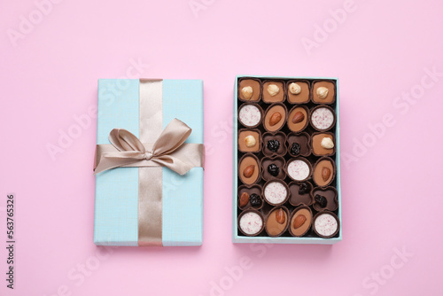 Open box of delicious chocolate candies on pink background, flat lay