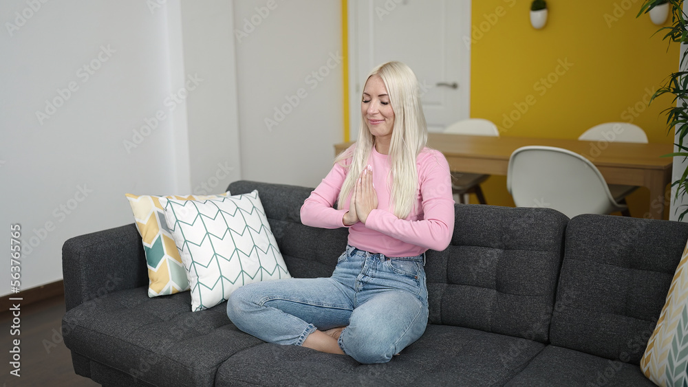 Obraz premium Young blonde woman doing yoga exercise sitting on sofa at home