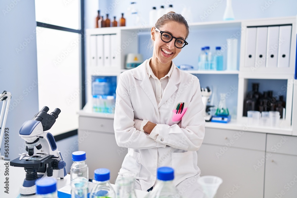 Young woman working at scientist laboratory happy face smiling with crossed arms looking at the camera. positive person.
