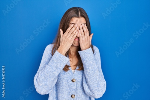 Young woman standing over blue background rubbing eyes for fatigue and headache, sleepy and tired expression. vision problem