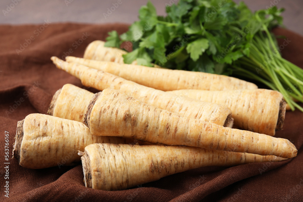 Whole raw parsley roots and fresh herb on brown fabric, closeup Whole raw parsley roots and fresh herb on brown fabric, closeup
