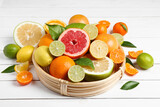 Different ripe citrus fruits with green leaves on white wooden table