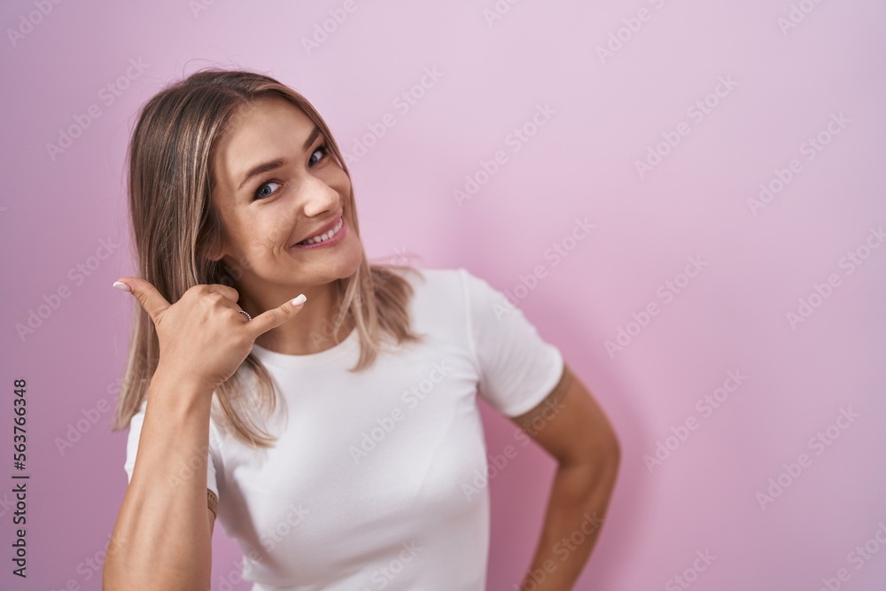 Blonde caucasian woman standing over pink background smiling doing phone gesture with hand and fingers like talking on the telephone. communicating concepts. Blonde caucasian woman standing over pink background smiling doing phone gesture with hand and fingers like talking on the telephone. communicating concepts.