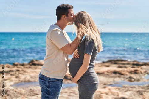 Man and woman couple standing together touching belly kissing at seaside