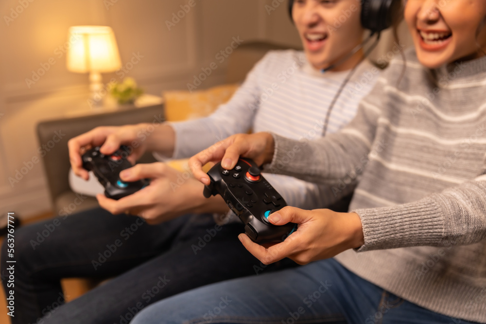 Emotional positive young asian family couple playing online video games. They Plays with Wireless Controllers. Cozy Room is Lit with Warm. Emotional positive young asian family couple playing online video games. They Plays with Wireless Controllers. Cozy Room is Lit with Warm.