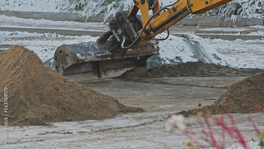 Fototapeta premium Industrial Excavator Scoop Distributing Sand on Street Surface During Winter Maintenance Roadworks