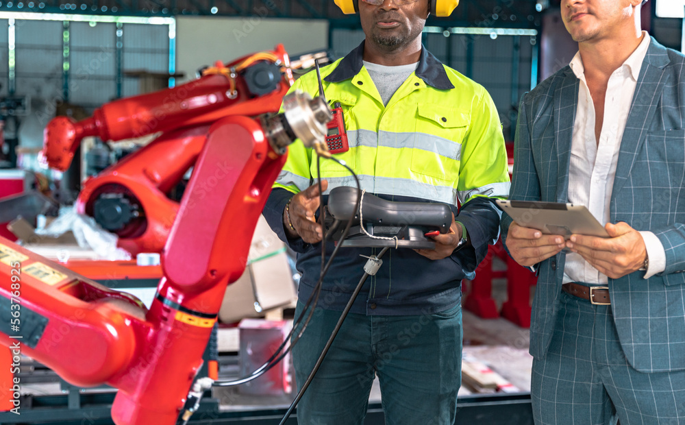 Business man and Factory engineer talking and shaking hands on business cooperation agreementAfrican American male engineer worker using tablet with the automatic robotic machine in the factory. Business man and Factory engineer talking and shaking hands on business cooperation agreementAfrican American male engineer worker using tablet with the automatic robotic machine in the factory.