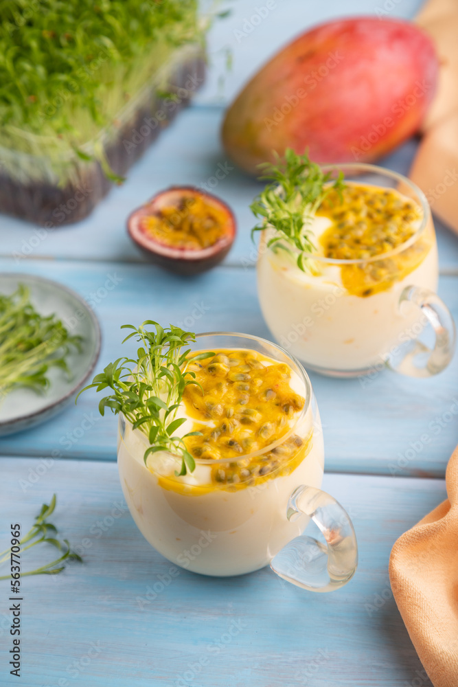 Mango yogurt with passionfruit and cilantro microgreen in glass on blue. Side view, selective focus. Mango yogurt with passionfruit and cilantro microgreen in glass on blue. Side view, selective focus.