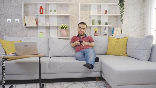 Positive disabled dwarf young man at home happily looking at phone smiling and resting.
Happy and cheerful young dwarf man looking at phone and resting on sofa in living room at home.
 photo