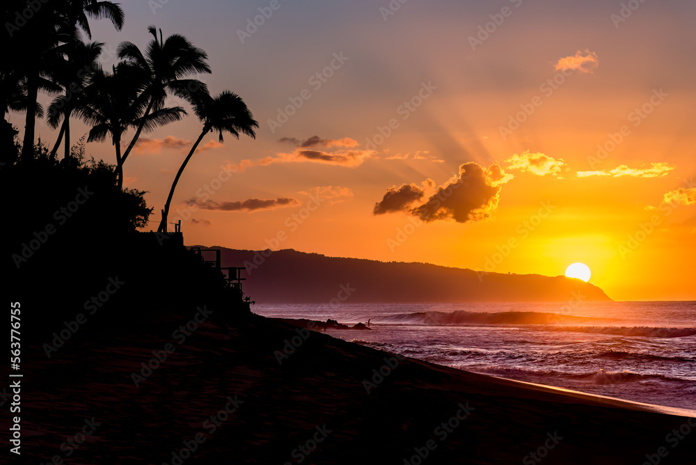 Sun setting behind the mountain over waves and palm trees on Sunset Beach, Hawaii