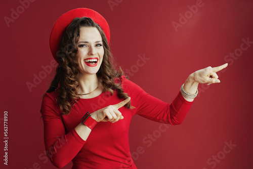happy stylish woman pointing at something on red background