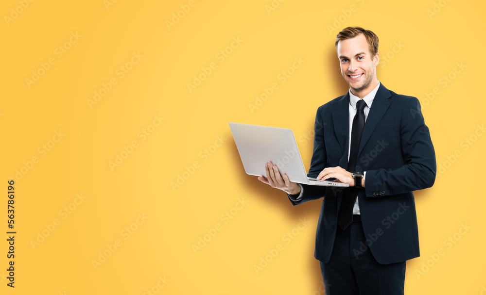 Happy smiling businessman in black confident suit, working with laptop, on vivid yellow background. Handsome young man at studio concept picture. Copy space for ad text. Happy smiling businessman in black confident suit, working with laptop, on vivid yellow background. Handsome young man at studio concept picture. Copy space for ad text.