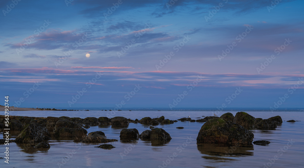 Obraz premium A seascape photo at sunrise with a full moon hanging in sky