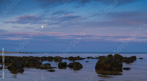 A seascape photo at sunrise with a full moon hanging in sky