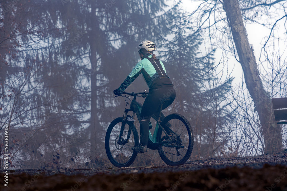 Beautiful mystic wood with fog and silhouettes of trees and female mountain biker at local mountain Uetliberg at Christmas Day. Photo taken December 25th, 2022, Zurich, Switzerland.
