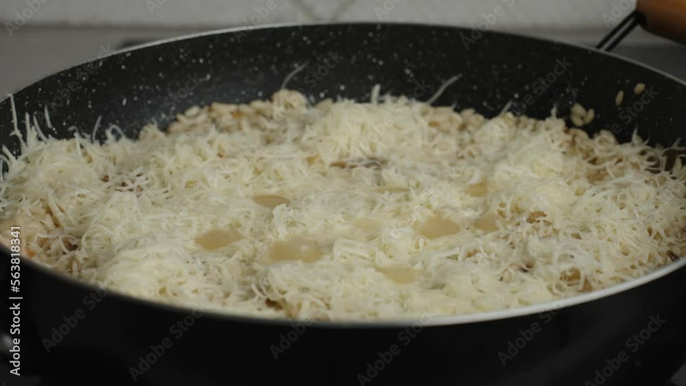 Process of cooking risotto with mushrooms. Arborio rice boiles in grying pan with grated cheese, close up. Italian cuisine dish