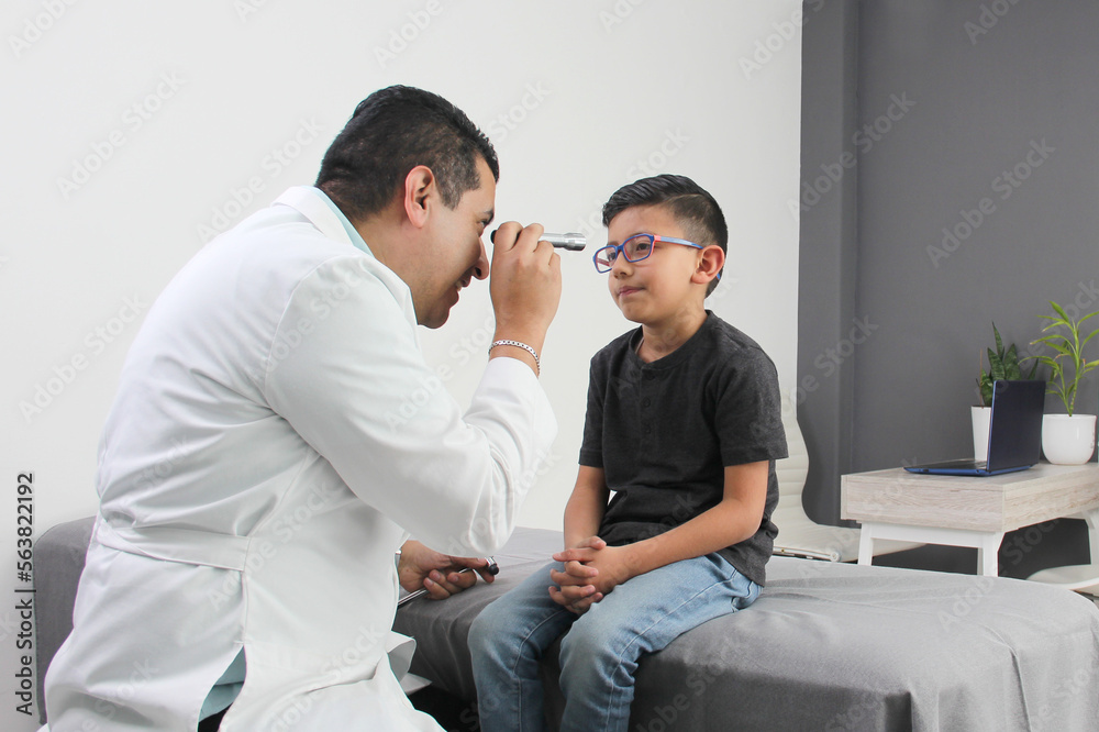 Professional specialist pediatrician doctor and patient 7-year-old Latino brown-haired boy are in consultation to check their eyes, mouth and throat to diagnose any disease in the office Professional specialist pediatrician doctor and patient 7-year-old Latino brown-haired boy are in consultation to check their eyes, mouth and throat to diagnose any disease in the office
