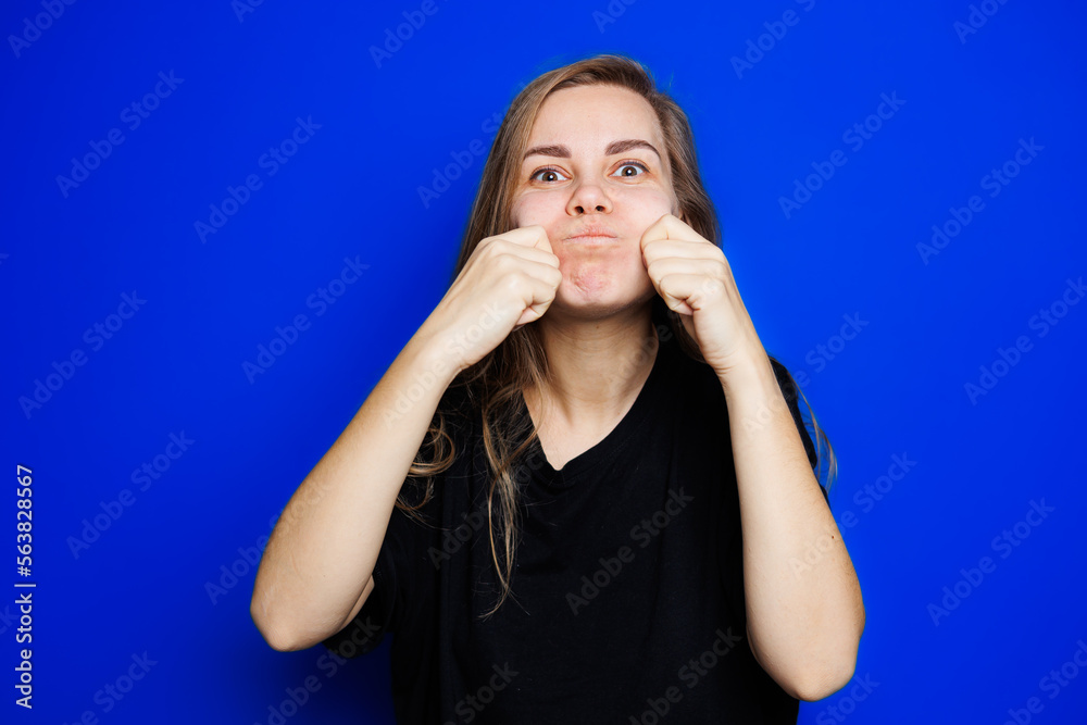 Happy beautiful woman without makeup in a black t-shirt showing different emotions on a blue background. Natural female beauty without cosmetics, naturalness. The concept of beauty Happy beautiful woman without makeup in a black t-shirt showing different emotions on a blue background. Natural female beauty without cosmetics, naturalness. The concept of beauty