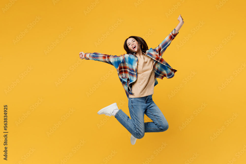 Full body young fun carefree overjoyed woman wear blue shirt beige t-shirt jump high with outstretched hands look camera isolated on plain yellow background studio portrait. People lifestyle concept. Full body young fun carefree overjoyed woman wear blue shirt beige t-shirt jump high with outstretched hands look camera isolated on plain yellow background studio portrait. People lifestyle concept.