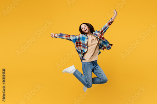 Full body young fun carefree overjoyed woman wear blue shirt beige t-shirt jump high with outstretched hands look camera isolated on plain yellow background studio portrait. People lifestyle concept.