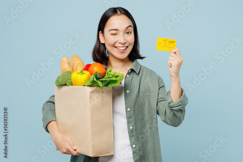 Young amazed fun woman wears casual clothes hold brown paper bag with food products credit bank card isolated on plain blue cyan background studio portrait. Delivery service from shop or restaurant.