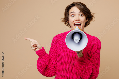 Surprised shocked young woman wear pink sweater hold in hand megaphone scream announces discount sale Hurry up isolated on plain pastel light beige background studio portrait People lifestyle concept