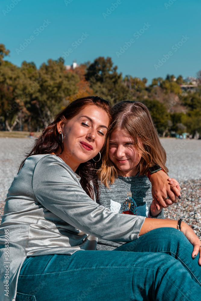 Mom and daughter are sitting hugging on the beach. Mom and daughter are sitting hugging on the beach.