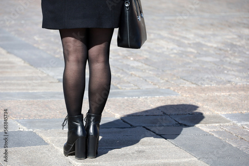 Girl in black stockings and shoes on high heels standing with handbag on a street, female fashion in spring city