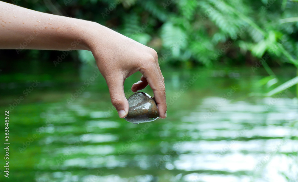 A woman's hand holding a zen basalt stone which she got from deep in the clear river water A woman's hand holding a zen basalt stone which she got from deep in the clear river water