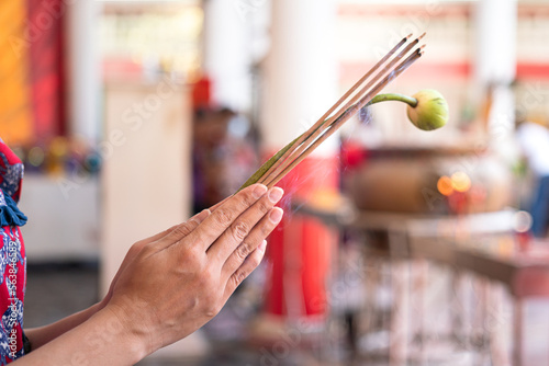 Action of human hand is holding incense stick and lotus flower during pay homage at the temple in Chinese new year event. Close-up and selective focus.