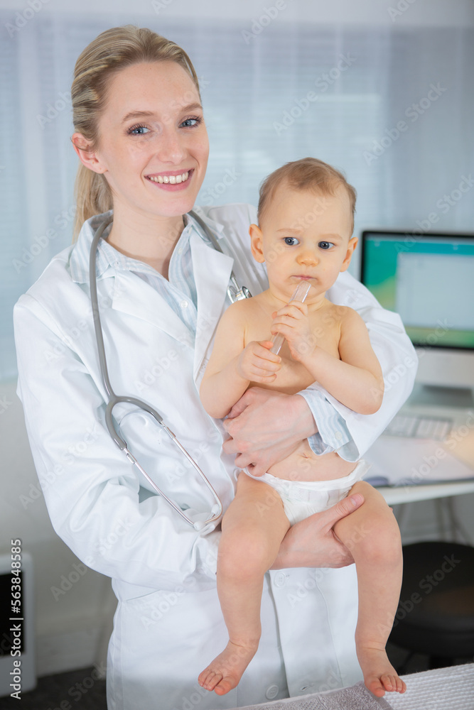 young joyful doctor holding baby and smiling in hospital young joyful doctor holding baby and smiling in hospital