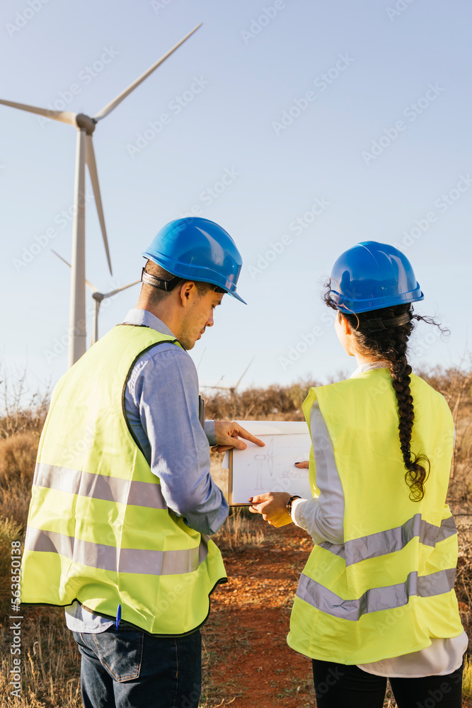 Engineers discussing over blueprint and wind turbines Engineers discussing over blueprint and wind turbines