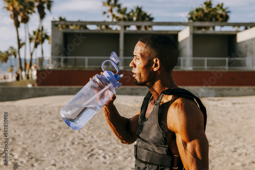 Thirsty sportsman standing with water bottle at beach