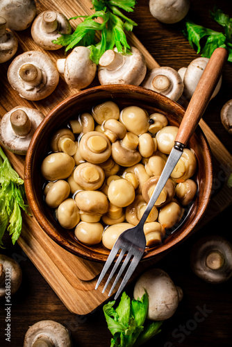 Pickled mushrooms in a bowl on a cutting board with greens. 