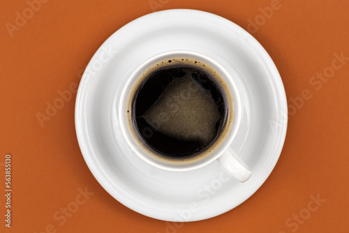 Coffee cup and saucer on brown background, flat lay.