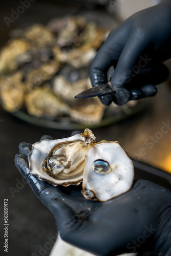 the chef holds an open oyster with a knife in his hands 
