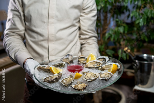 open oysters in a large dish on ice in the hands of a waiter on a green background
