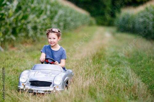 Little preschool kid girl driving big toy car and having fun with driving in nature