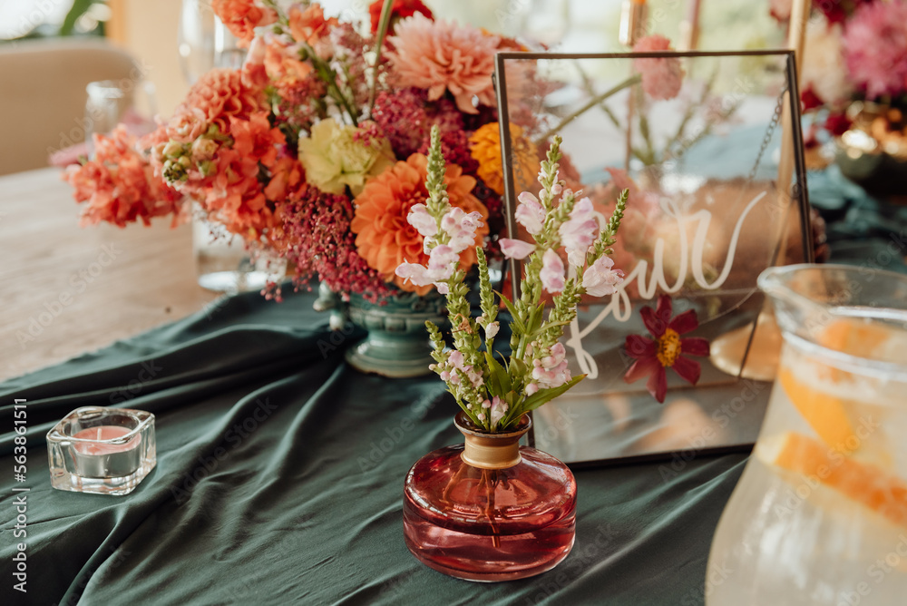 Detail of a table setting in a restaurant. Fresh flowers in a small vase on a green tablecloth. Next to the flowers is a candle in a glass candlestick. Detail of a table setting in a restaurant. Fresh flowers in a small vase on a green tablecloth. Next to the flowers is a candle in a glass candlestick.