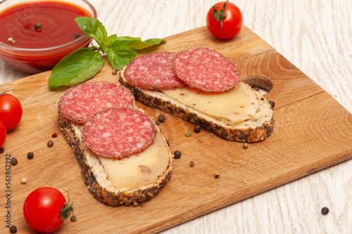 Sandwiches with smoked sausage and cheese on a wooden board decorated with cherry tomatoes and basil