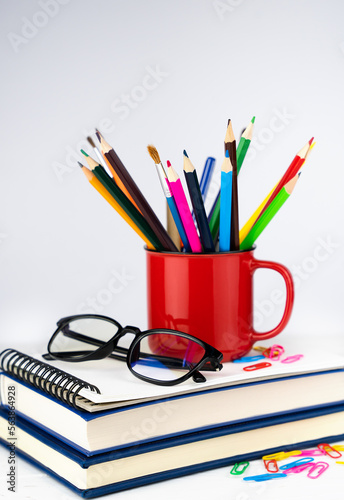 Pencils in a bright red mug and the books. School concept. Teacher's Day. Selective focus.