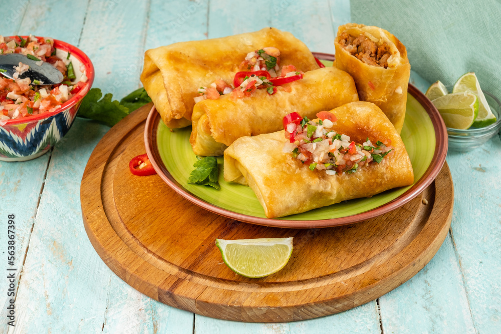 Chimichanga or burrito on a green plate with salsa sauce. Mexican traditional snack. Chimichanga or burrito on a green plate with salsa sauce. Mexican traditional snack.