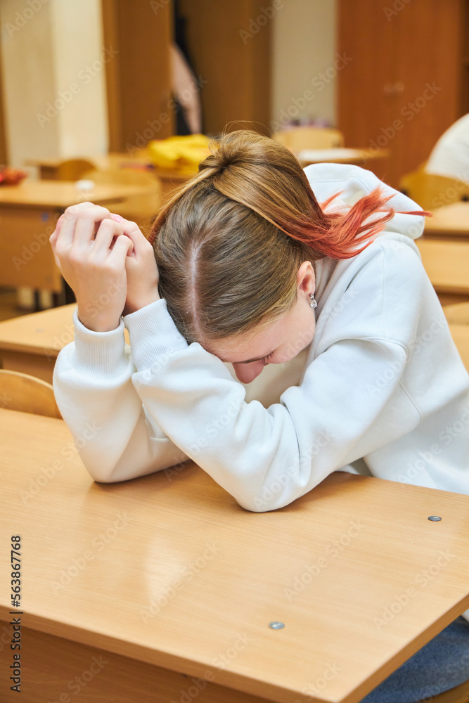 Fototapeta premium A teenage schoolgirl girl is sitting at a desk at school. Boredom in class