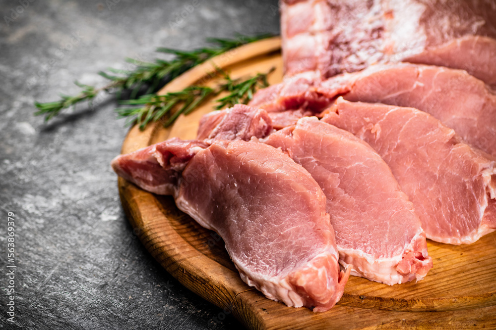 Fresh raw pork on a cutting board with rosemary.