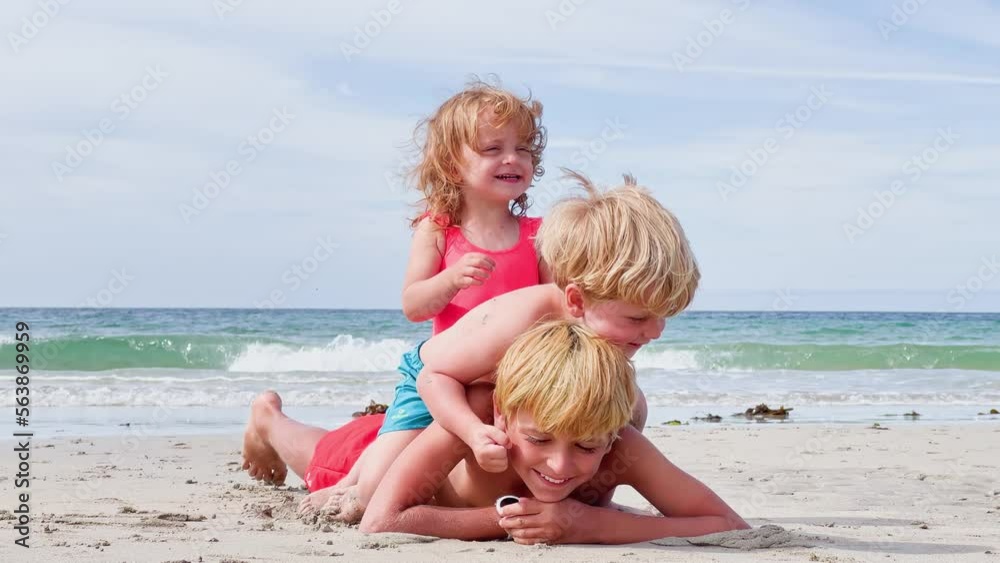 Three kids lay on top of another at the sand sea beach Three kids lay on top of another at the sand sea beach