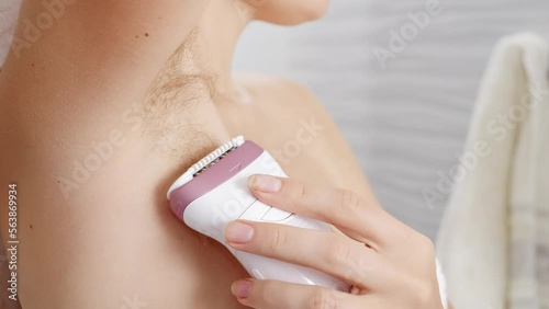 Closeup of young woman with long armpit hair making depilation with electric epilator. Concept of hygiene, natural beauty, feminity and body hair growth