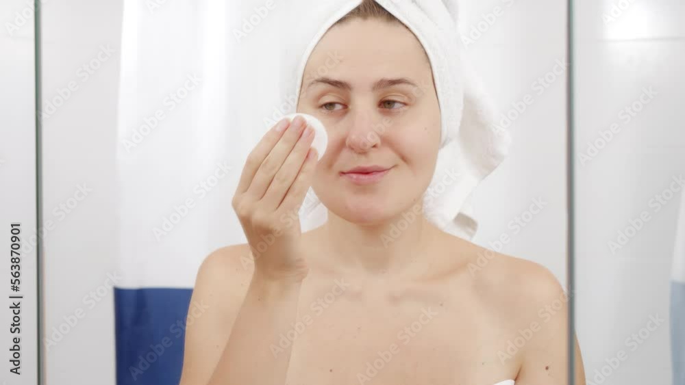 Young woman cleaning face with cotton pad and cleanser in bathroom. Concept of beautiful female, makeup at home, skin care and domestic beauty industry. Young woman cleaning face with cotton pad and cleanser in bathroom. Concept of beautiful female, makeup at home, skin care and domestic beauty industry.