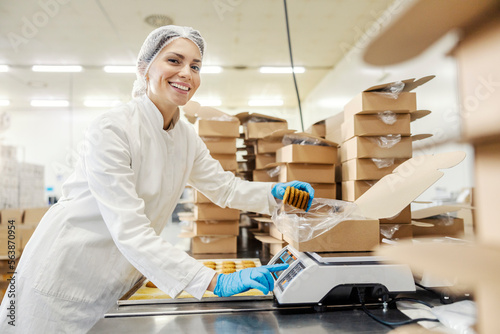 Canvastavla A happy food factory worker is measuring cookies on scales and putting them in a box